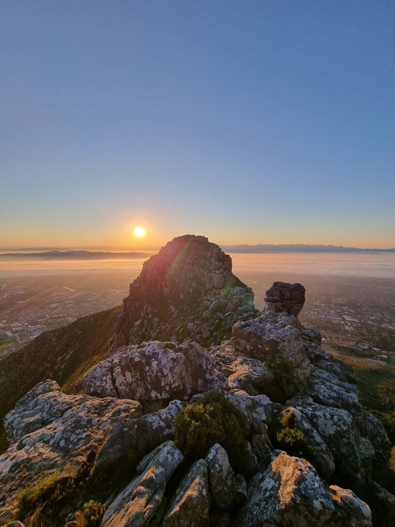 The sun rising behind a rocky summit, with flat land and the sea far below