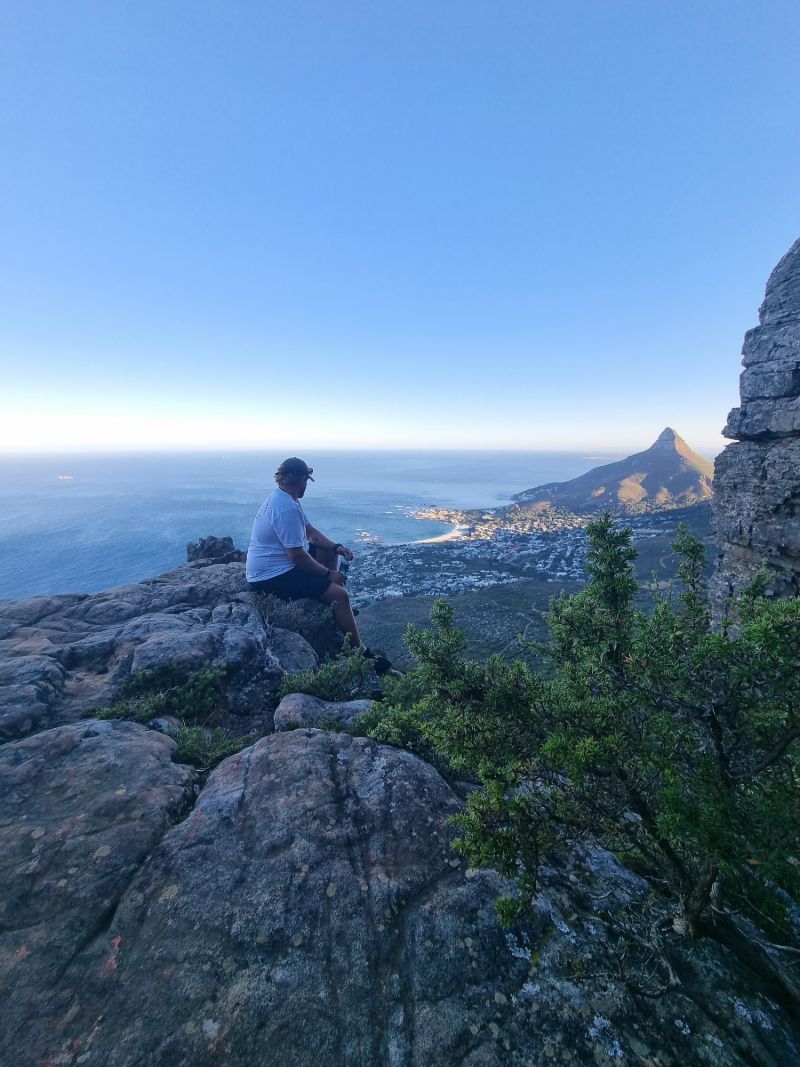 A hiker sitting on a rock ledge high above the Atlantic, with Lion's Head in the distance